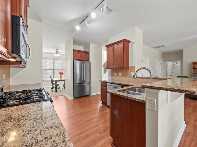 kitchen featuring light wood finished floors, tasteful backsplash, a peninsula, stainless steel appliances, and a sink