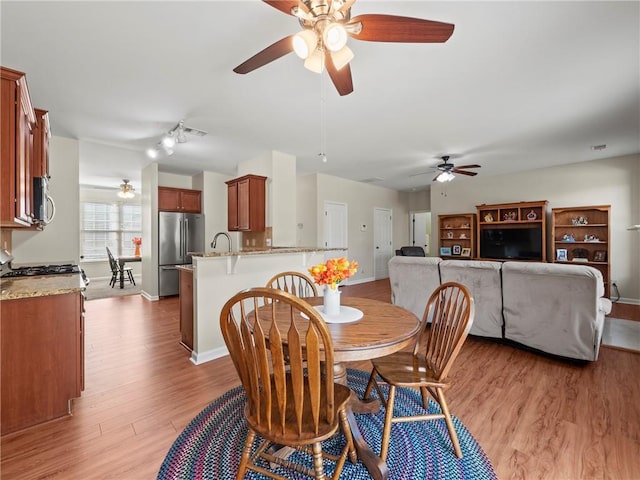 dining space with a ceiling fan, light wood-type flooring, visible vents, and baseboards