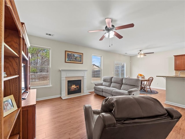 living room with light wood-type flooring, baseboards, visible vents, and a glass covered fireplace