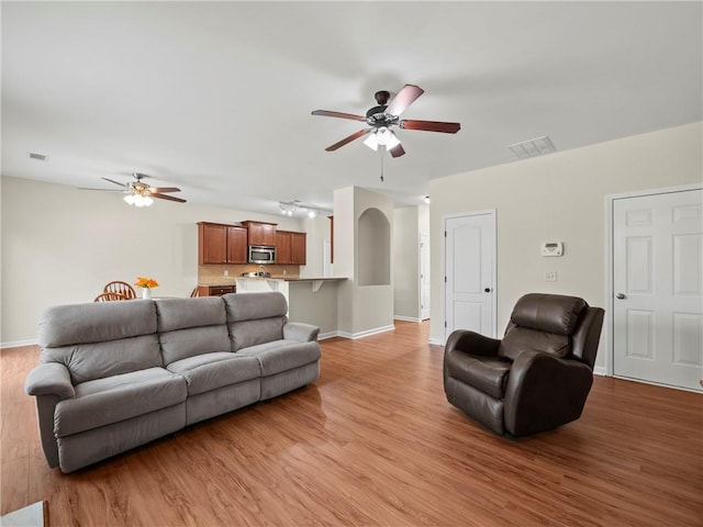 living area featuring light wood finished floors, baseboards, visible vents, and a ceiling fan