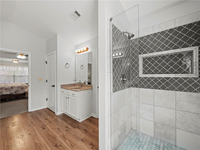 full bath featuring connected bathroom, wood finished floors, vanity, visible vents, and a tile shower