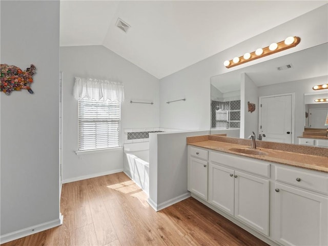 full bath with visible vents, lofted ceiling, wood finished floors, a garden tub, and vanity