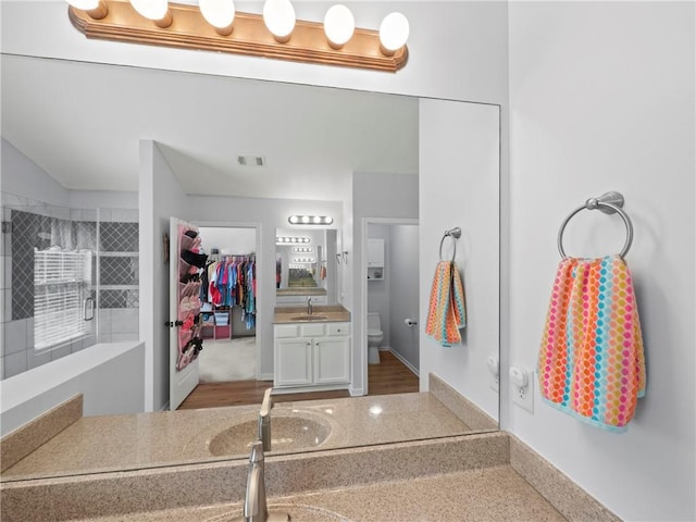 full bath with toilet, visible vents, a tile shower, and vanity