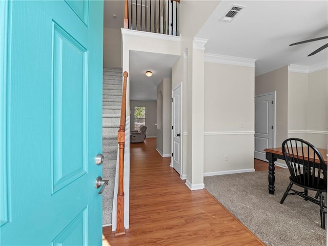 foyer with visible vents, a ceiling fan, light wood-style flooring, stairs, and crown molding