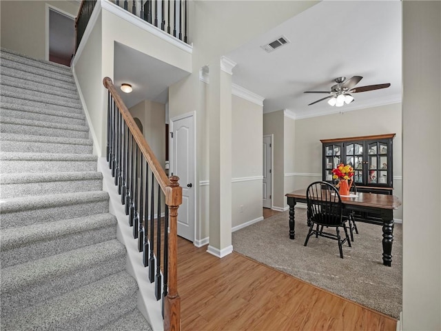 staircase with ornamental molding, wood finished floors, visible vents, and a ceiling fan