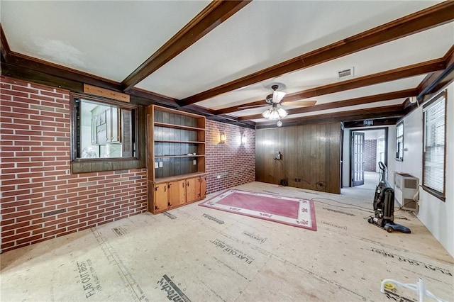 unfurnished living room with beamed ceiling, ceiling fan, and brick wall