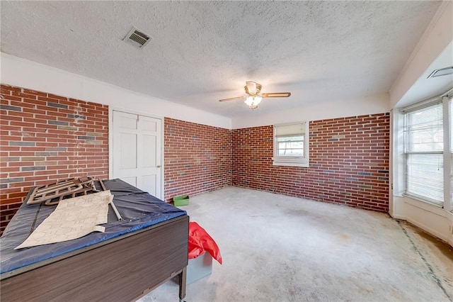 miscellaneous room with plenty of natural light, brick wall, and a textured ceiling