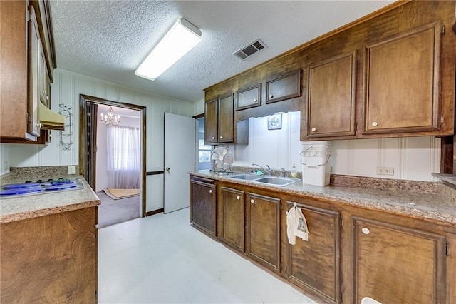 kitchen featuring a chandelier, custom range hood, stainless steel gas stovetop, sink, and a textured ceiling