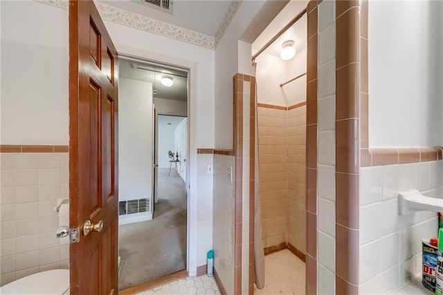 bathroom with tile walls, toilet, and tiled shower