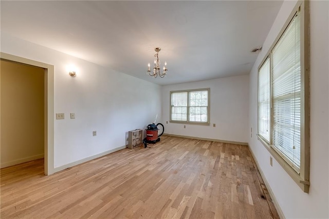 unfurnished room featuring a notable chandelier and light wood-type flooring