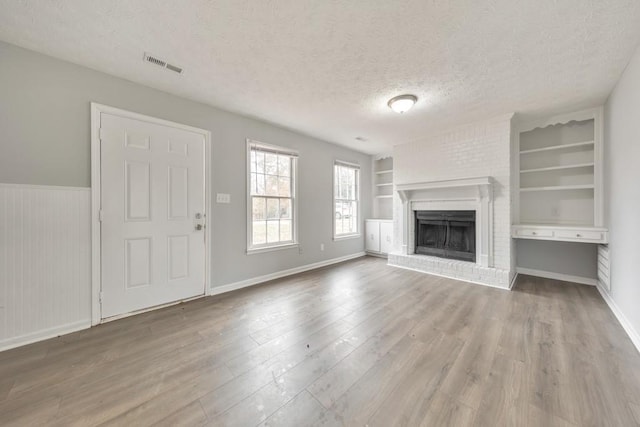 unfurnished living room with a brick fireplace, hardwood / wood-style floors, built in features, and a textured ceiling