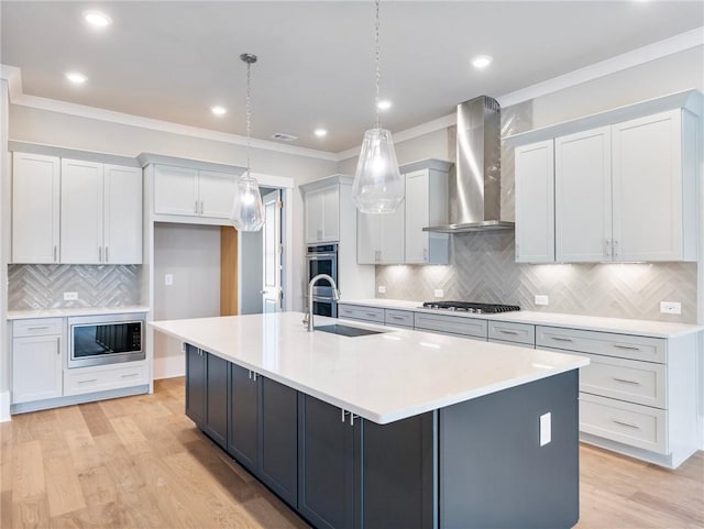 kitchen with a kitchen island with sink, wall chimney range hood, stainless steel appliances, and hanging light fixtures