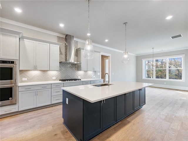 kitchen featuring sink, wall chimney exhaust hood, decorative light fixtures, and a center island with sink