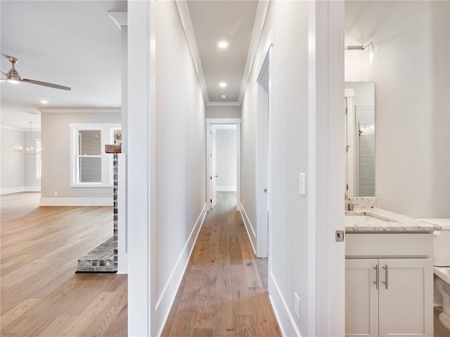 hall with light wood-type flooring, ornamental molding, and sink