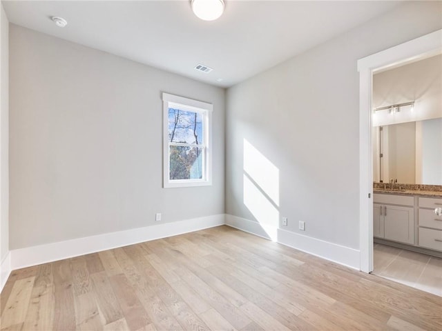 unfurnished bedroom featuring ensuite bathroom, sink, and light hardwood / wood-style flooring