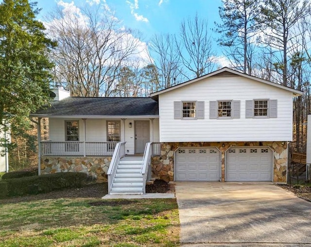 tri-level home with stone siding, a garage, driveway, covered porch, and a chimney