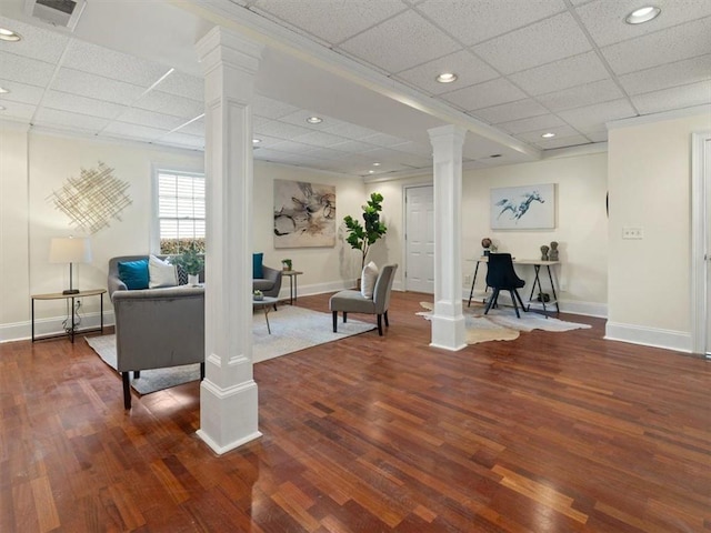 living area featuring ornate columns, a drop ceiling, baseboards, wood finished floors, and recessed lighting