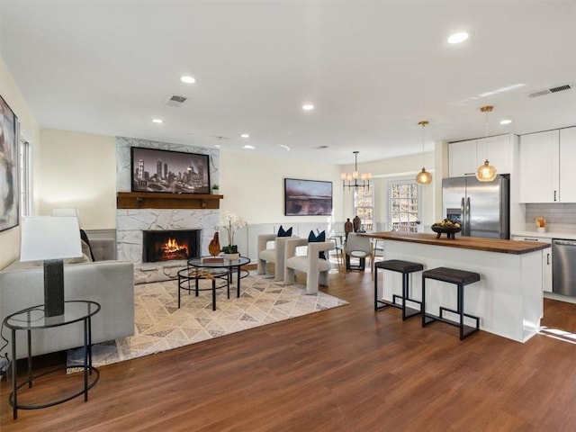 living room with a stone fireplace, dark wood-type flooring, recessed lighting, and a chandelier
