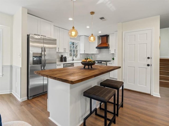 kitchen featuring wooden counters, appliances with stainless steel finishes, wall chimney range hood, dark wood-style flooring, and recessed lighting
