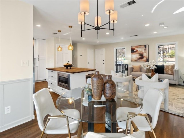 dining area with a chandelier, dark wood-type flooring, recessed lighting, and wainscoting