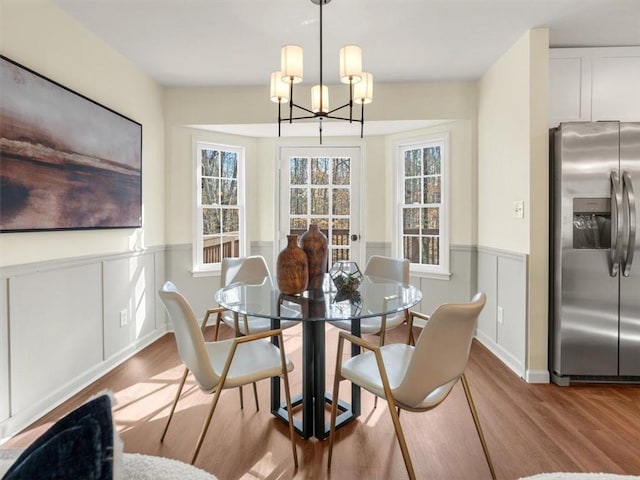 dining area with wood finished floors, a chandelier, and a wainscoted wall