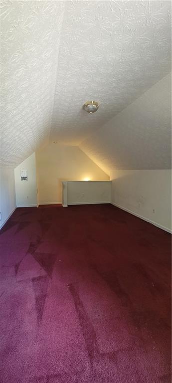 2703 Hillvale Cove Dr, Lithonia, GA 30058 - additional living space with vaulted ceiling, dark carpet, and a textured ceiling