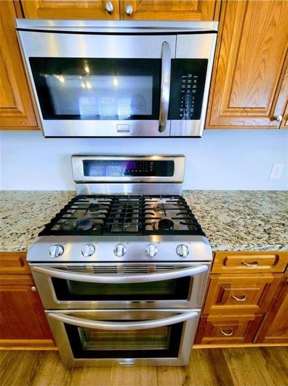 3735 Fir Dr, Buford, GA 30518 - kitchen with brown cabinets, wood finished floors, light stone counters, and appliances with stainless steel finishes