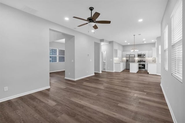 unfurnished living room with dark wood-style floors, recessed lighting, baseboards, and ceiling fan with notable chandelier