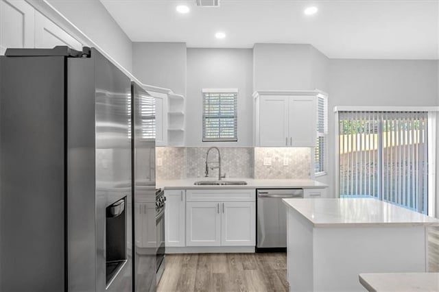 kitchen featuring tasteful backsplash, light wood-style flooring, stainless steel appliances, white cabinetry, and a sink