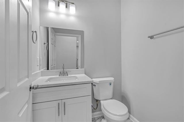 half bath with toilet, marble finish floor, baseboards, and vanity