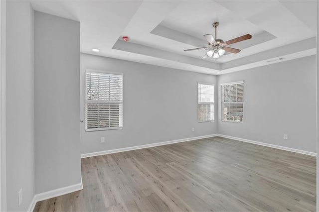 unfurnished room with a tray ceiling, baseboards, and wood finished floors