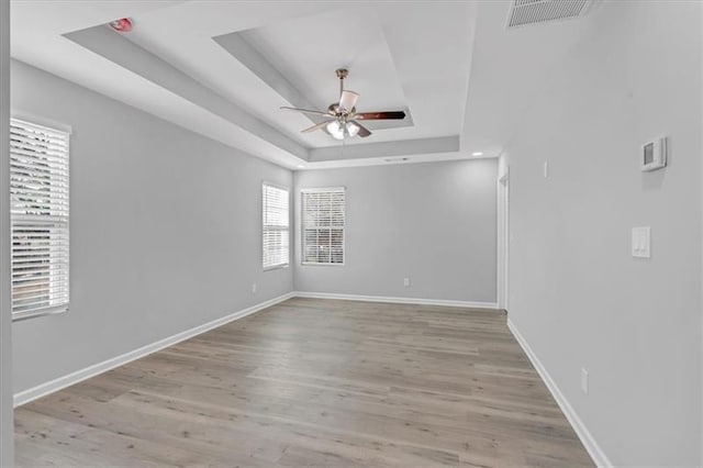 spare room featuring a raised ceiling, visible vents, a ceiling fan, wood finished floors, and baseboards