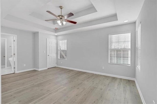 empty room featuring baseboards, a tray ceiling, a ceiling fan, and light wood-style floors