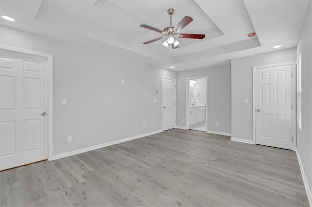 unfurnished bedroom featuring ensuite bath, baseboards, a raised ceiling, and wood finished floors