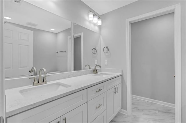 bathroom featuring double vanity, marble finish floor, baseboards, and a sink