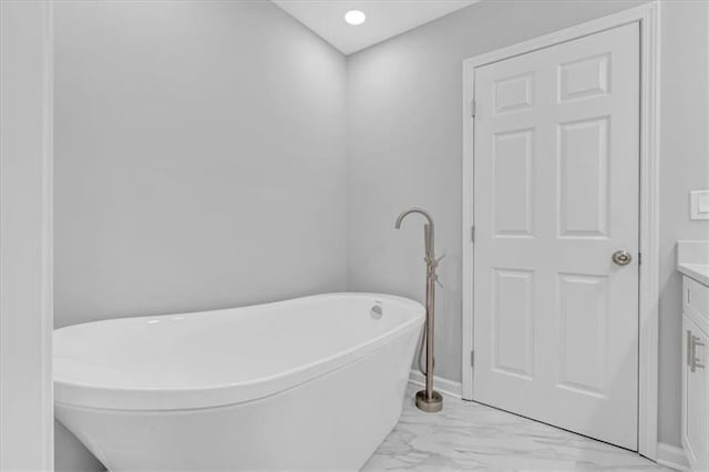 full bath featuring marble finish floor, a freestanding tub, vanity, and baseboards