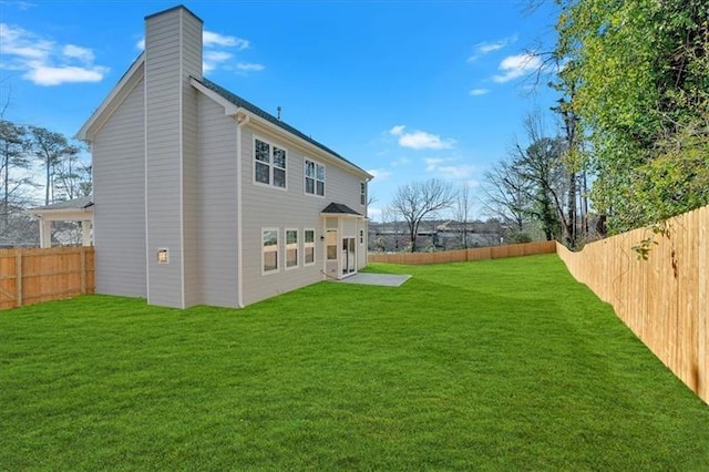 rear view of property with a lawn, a chimney, and a fenced backyard