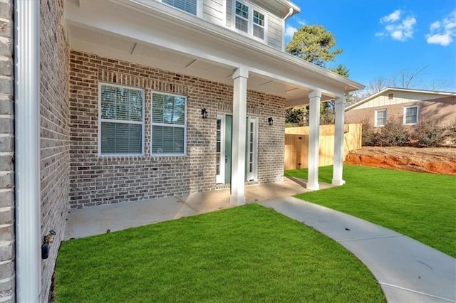 doorway to property featuring a patio, brick siding, and a lawn