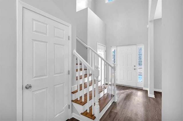 foyer entrance with stairway, wood finished floors, a towering ceiling, and baseboards