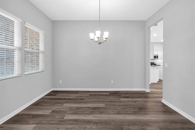 unfurnished dining area featuring dark wood-type flooring, a notable chandelier, and baseboards