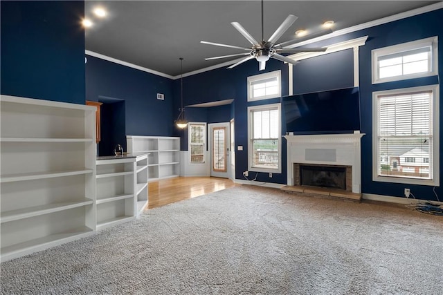 unfurnished living room featuring carpet floors, ornamental molding, a glass covered fireplace, and a towering ceiling