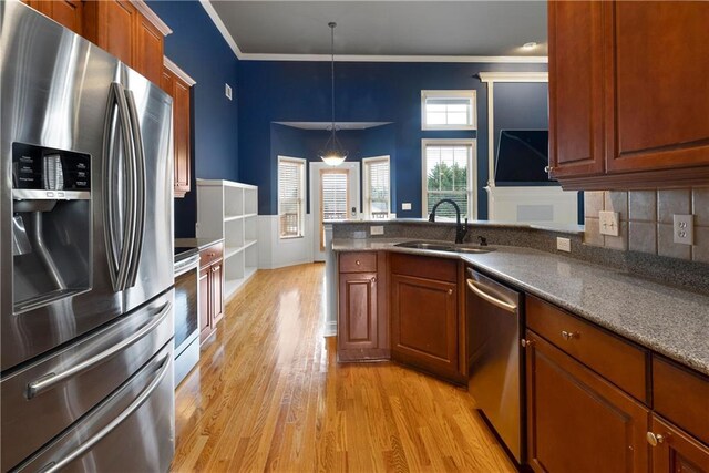 kitchen featuring light wood-style flooring, a peninsula, a sink, appliances with stainless steel finishes, and brown cabinets