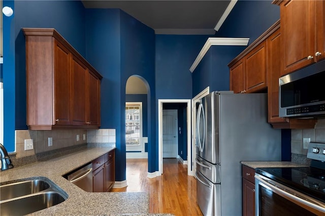 kitchen featuring arched walkways, light wood finished floors, stainless steel appliances, tasteful backsplash, and a sink