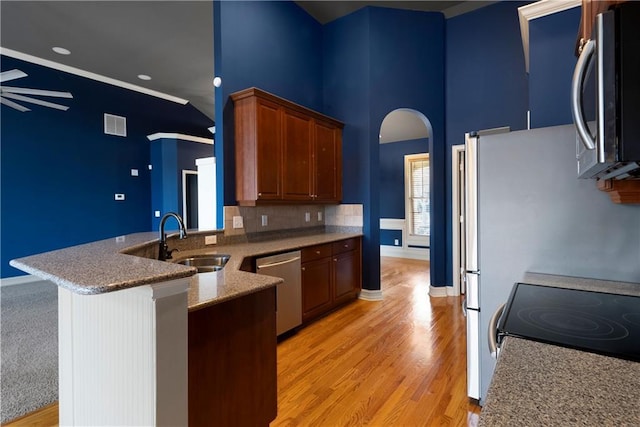 kitchen featuring arched walkways, light wood-style flooring, a peninsula, stainless steel appliances, and a sink