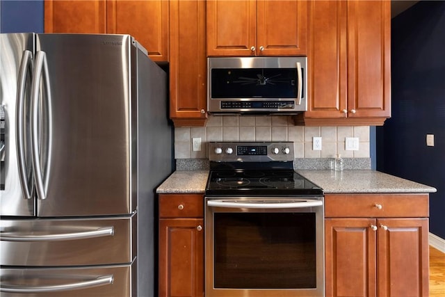 kitchen with stainless steel appliances, brown cabinetry, backsplash, and light stone countertops