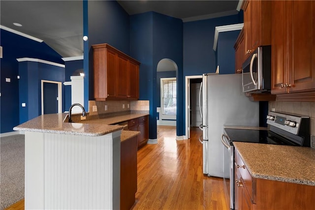 kitchen with stainless steel appliances, a peninsula, ornamental molding, backsplash, and brown cabinetry