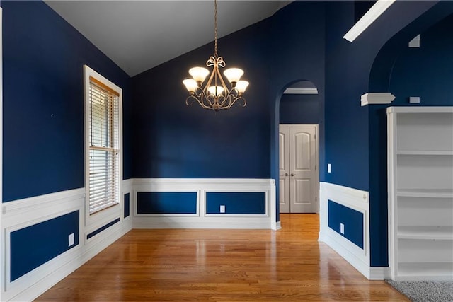 unfurnished dining area featuring built in features, lofted ceiling, a wainscoted wall, wood finished floors, and a notable chandelier