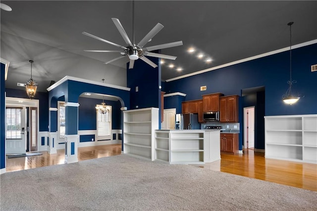 kitchen with arched walkways, ceiling fan with notable chandelier, stainless steel appliances, open floor plan, and brown cabinetry