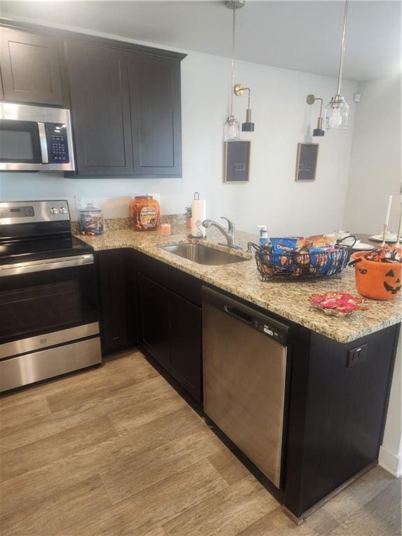 kitchen featuring a sink, light stone countertops, a peninsula, stainless steel appliances, and light wood-style floors