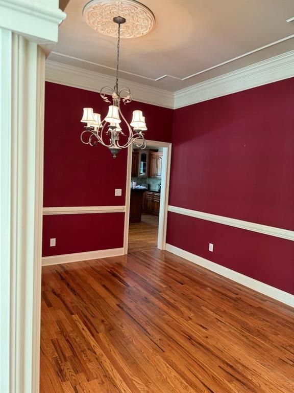 unfurnished dining area with hardwood / wood-style flooring, crown molding, and a notable chandelier